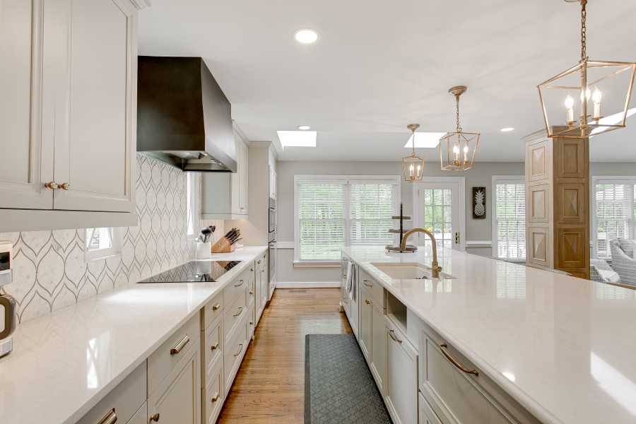 Luxury interior staged kitchen white stone countertops decor stools ceramic tile backsplash modern brass light pendants wood columns for a waldorf maryland home.