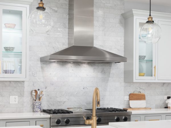 A beautiful modern kitchen with grey and blue cabinets, stainless steel appliances, gold hardware and glass lights hanging above the large island. No brands or labels.