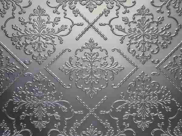 Closeup of an embossed silver glass panel. Intricate floral and geometric patterns are etched into the surface, creating a textured, decorative effect. The design is symmetrical and repetitive.