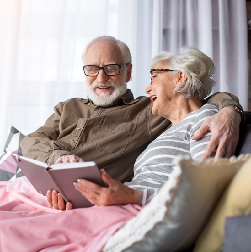 Happy moments. Portrait of serene charming husband and wife resting at living room. Man is showing woman funny picture while they are laughing and enjoying memories